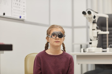Portrait of cute little girl wearing trial frame during vision test in pediatric ophthalmology...