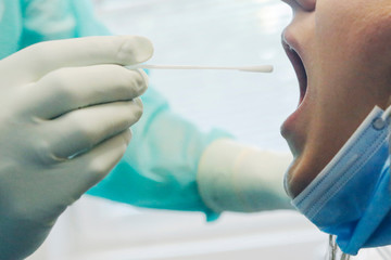 Medical in protective clothing takes COVID-19 swab test tube from mouth at Covid-19 test center...