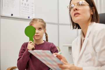 Portrait of cute little girl reading test chart during vision test in pediatric ophthalmology clinic, copy space