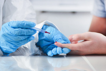 Coronavirus test. Blood sampling on Covid-19. Doctor’s hands in gloves and patient’s hands with a drop of blood on a finger, on a light background, close-up.Collection of biological material