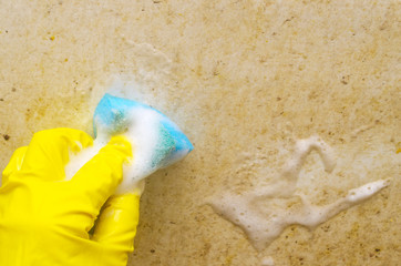 A man in a yellow protective glove washes a very dirty bath with a blue sponge..Regular domestic cleaning in bathroom.