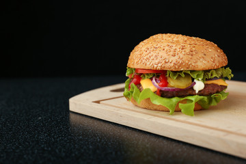  classic american burger on wooden board on black background with copy space
