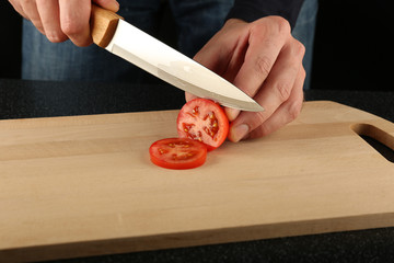 cook cuts tomatoes on a cutting board on a black background