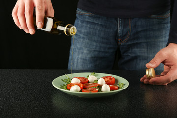 olive oil flows from the bottle on a salad with mozzarella cheese, arugula and tomatoes