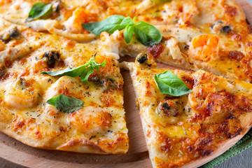 Seafood thin tasty pizza with shrimps, mussels and basil on wooden background