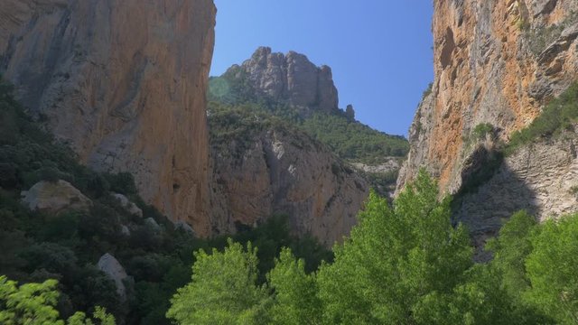 AERIAL DRONE TACK OFF AND FORWARD MOVEMENT TOWARDS ROCKY MOUNTAIN WALLS. GREEN PINES AND CLAY ROCKS