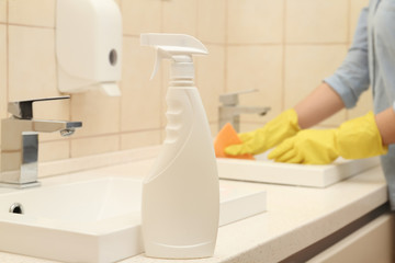 Woman cleaning sink in bathroom, focus on bottle of detergent