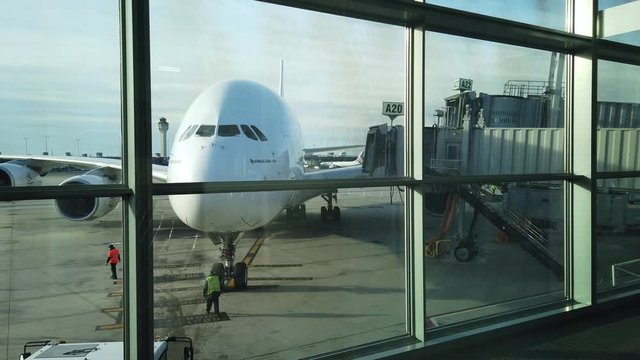 Huge plane at gate for service as ground crew begins to work after arrival. Plane with two levels parked at gate. Jetway extending toward aircraft for passengers to disembark or deplane.
