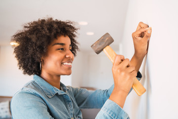 Afro woman hammering nail on the wall. Stay at home concept.