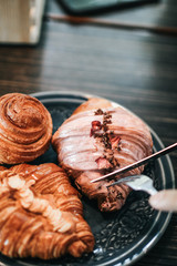 Hands prepare for eating fresh sweet bake croissant almond by use a fork and knife for cutting on a black plate for breakfast over on dark wooden table background morning time.copy space for your text