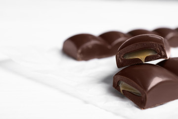 Pieces of chocolate with caramel filling on white table, closeup. Space for text