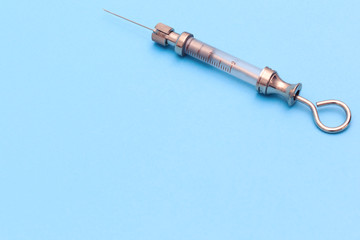 antique syringe made of metal and glass on a blue background. free space for text. copyspace
