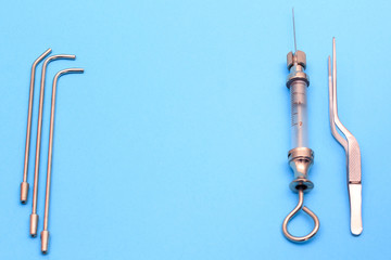 vintage syringe for intrauterine infusions and tonsillectomy on a blue background. a pair of medical tweezers and a syringe are next to it. copyspace