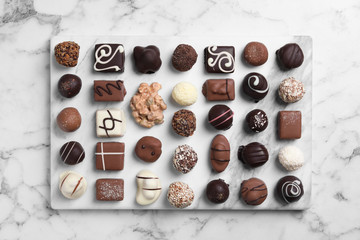 Different tasty chocolate candies on white marble table, flat lay