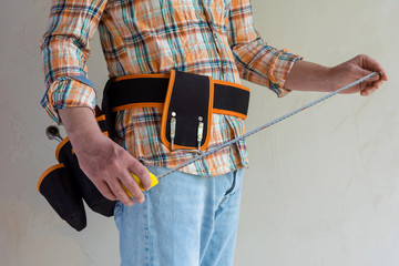 The Builder measures the length with a tape measure.