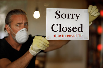 coronavirus closed for business concept, male business owner with medical mask puts sorry closed...