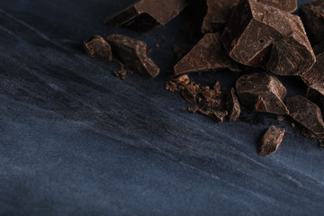 Pieces of dark chocolate on blue marble table, closeup. Space for text