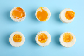 Different readiness stages of boiled chicken eggs on light blue background, flat lay