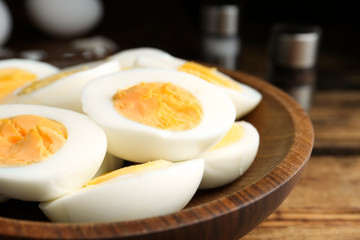 Cut hard boiled chicken eggs in wooden bowl on table, closeup