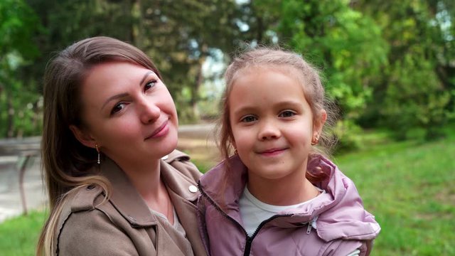Portrait of mother and a small daughter, spends time together in a city park.