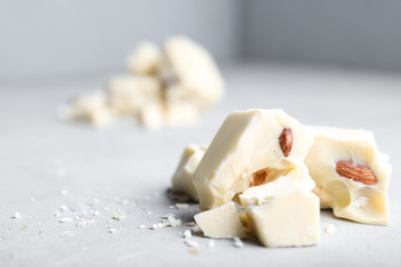 Fototapeta na wymiar Pieces of tasty white chocolate with nuts on light grey table, closeup. Space for text