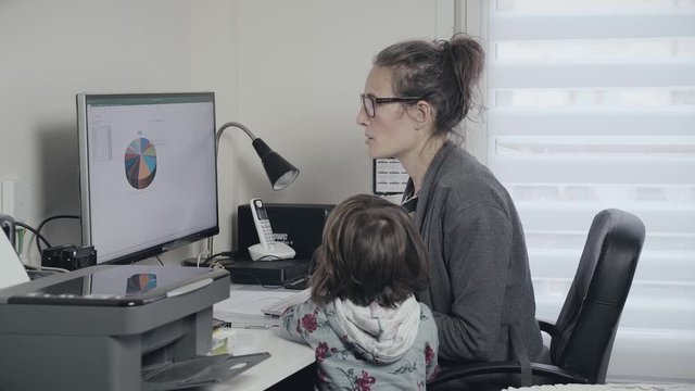 Caucasian woman working on computer at home is visited by small child, pan