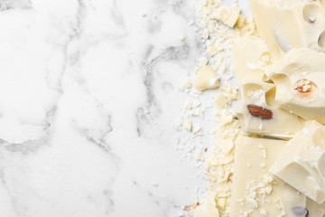 Pieces of tasty white chocolate with nuts on marble table, flat lay. Space for text