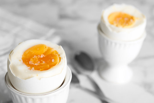 Tasty medium boiled egg in ceramic holder on white table, closeup