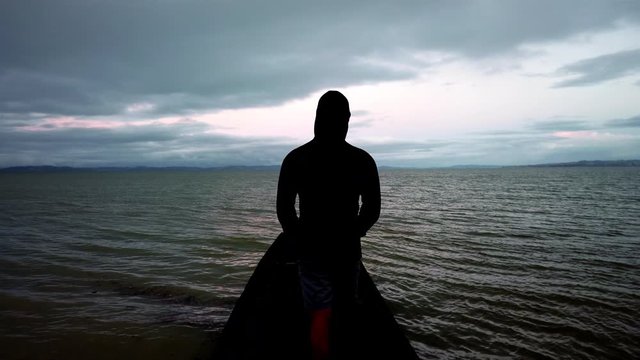 Hooded anonymous man walking on a pier in the middle of sea, silhouette, slowmo