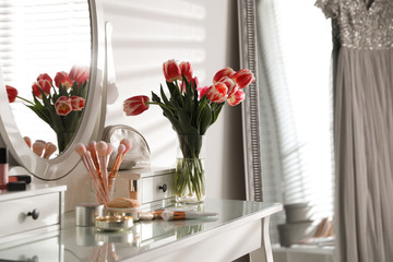Elegant dressing table with makeup products, accessories and tulips indoors. Interior element