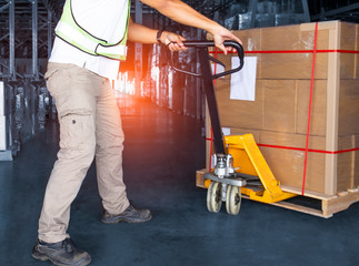 Warehouse worker unloading large pallet shipment goods, his using hand pallet truck, Interior of storage warehouse, manufacturing plant of shipping warehouse