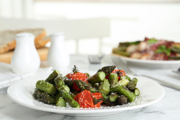Oven baked asparagus with cherry tomatoes on white plate