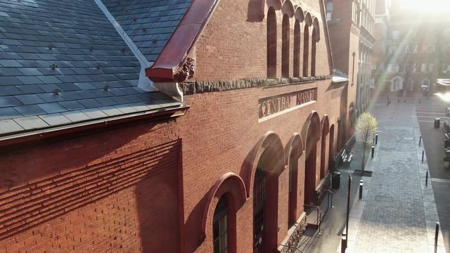 Brick central market building during dramatic morning sunlight, historic brick architecture, aerial drone pullback revealing shot of cobblestone street