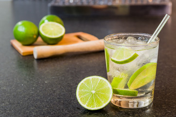 Caipirinha, traditional Brazilian alcoholic drink, typical drink made with sugar, lemon, distilled cane (cachaca) and ice. Ingredients and the drink on black granite surface.