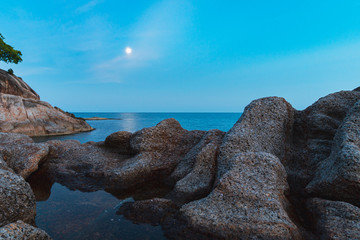 Fototapeta na wymiar Full moon at spectacular sunset over rocks and sea 