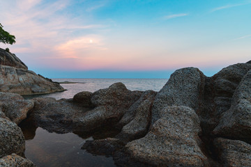 Full moon at spectacular sunset over rocks and sea 
