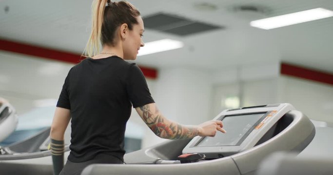 Young woman choosing workout routine on a treadmill at gym. Back view. Woman training at fitness center. Woman exercising cardio workout