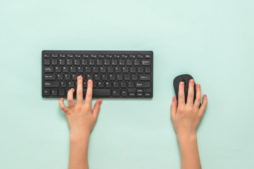 Hands of a child with a black keyboard and mouse on a light background.