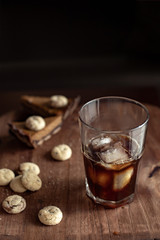 Transparent glass with cold coffee, sweets and cookies on a wooden table