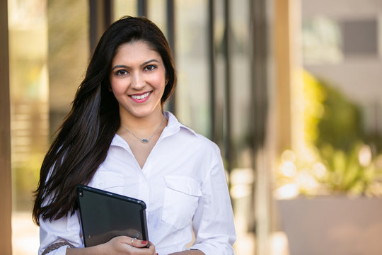 Portrait of a beautiful smiling cheerful female indian american successful business woman CEO entrepreneur at the workplace, standing confidently