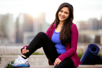 Portrait of a beautiful mixed ethnicity brunette woman in sportswear, sitting relaxed after a morning yoga workout with city skyline in the background