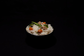 A bowl of rice with vegetables and soya chunks in a black copy space background. Food photography.