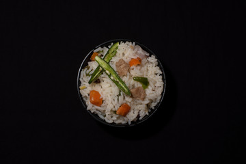 A bowl of rice with vegetables and soya chunks in a black copy space background. Food photography.