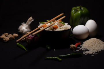 Obraz na płótnie Canvas A bowl of a steamed rice and vegetables decorated with veggies, eggs, grains, chopsticks and spoon in a black copy space background. Food photography.