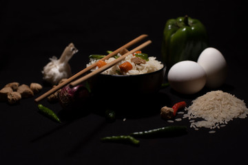 Obraz na płótnie Canvas A bowl of a steamed rice and vegetables decorated with veggies, eggs, grains, chopsticks and spoon in a black copy space background. Food photography.