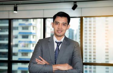 Fototapeta premium Portrait of happy man in suit and tie standing against city scape background. Confident successful smiling young business man executive with folded arms posing against a building background.