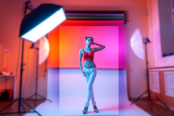 Photographing clothes for a catalog on a stylish thin woman in a photo studio with plain colors and bright pink neon lighting. Fashion shooting concept for a clothing store.