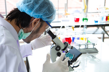 Asian doctor or scientist Laboratory wearing a face mask protect from virus is looking through a microscope to research for antiviral vaccine or medication on hospital lab background.