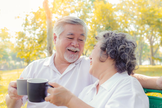 Senior couple drinking hot coffee or tea at park with happiness. Senior man and elderly woman hold cup of coffee and say cheers together for good health. Pensioner couple are laughing together at park