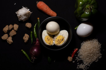 Top down image of a boiled eggs in a bowl decorated with cereals and vegetables in dark copy space background. Food and product photography.